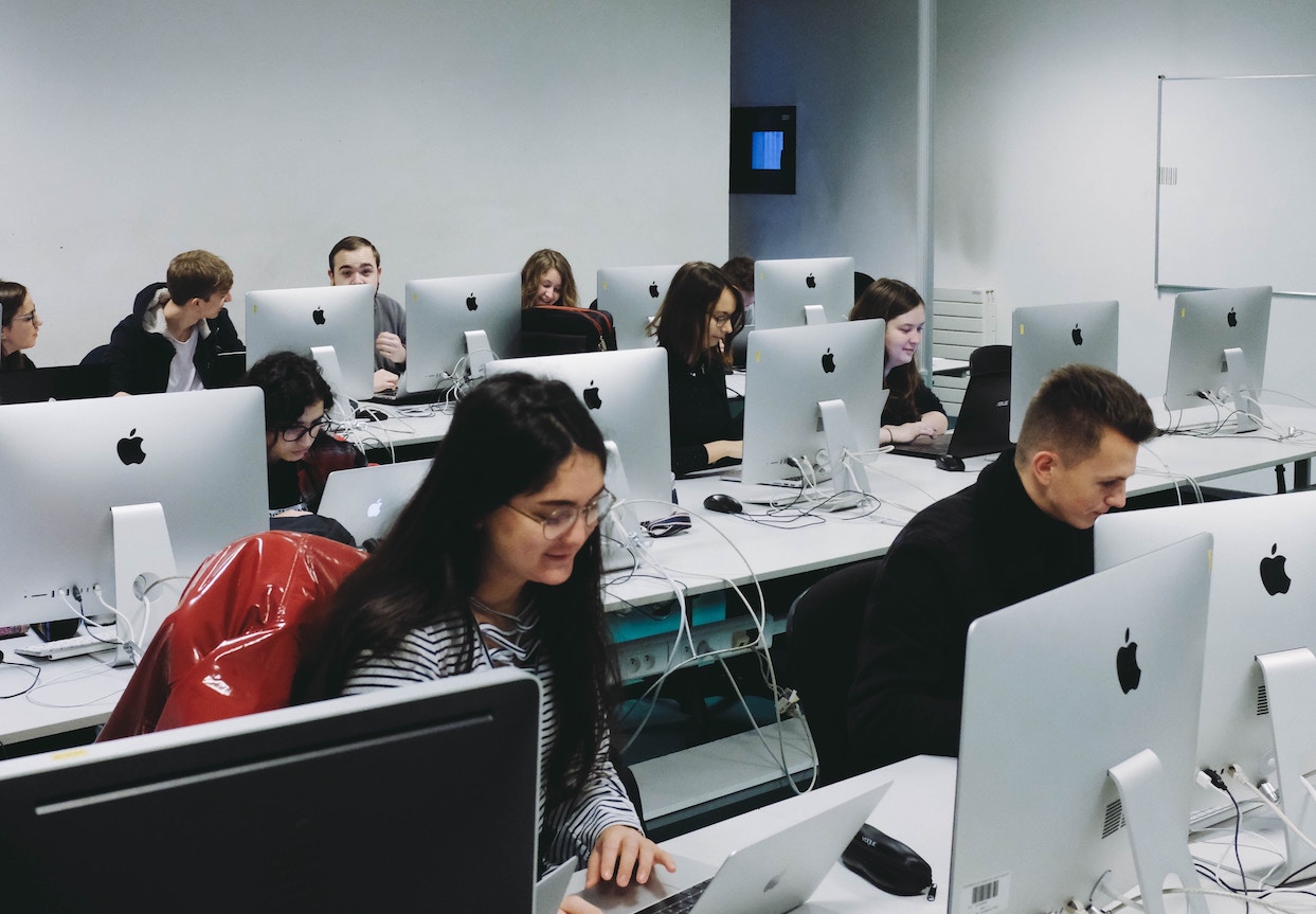 Three rows of people sitting in front of iMac all-in-one desktops