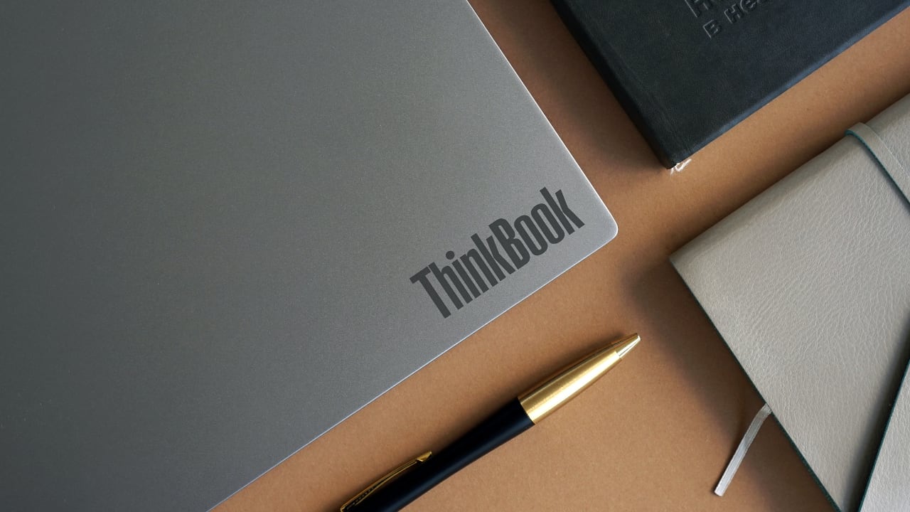Thinkbook laptop on brown desk with leather book and pen
